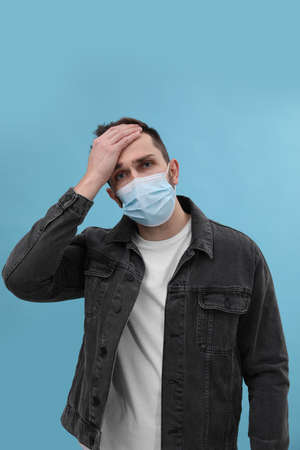 Man in mask suffering from headache on light blue background. cold symptomsの写真素材