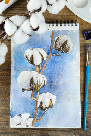 Painting of cotton flowers in sketchbook and art supplies on wooden table, flat layの写真素材