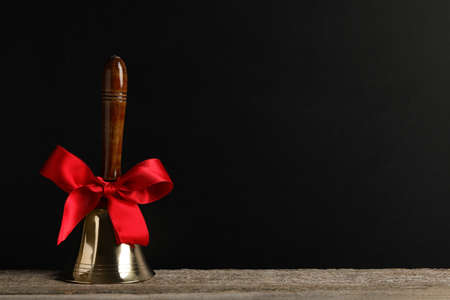 Golden bell with red bow on wooden table near blackboard, space for text. School daysの写真素材