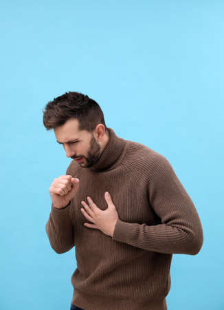 Man coughing on light blue background. cold symptomsの写真素材