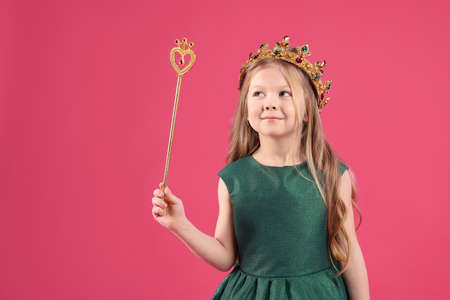 Cute girl in fairy dress and golden crown holding magic wand on pink background. little princess