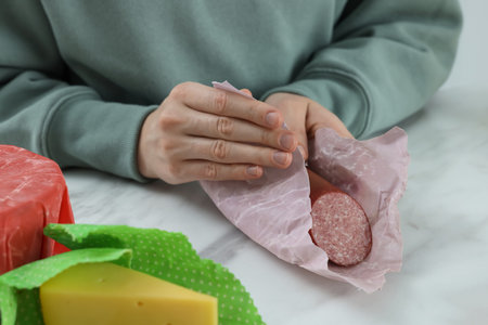 Woman packing tasty sausage into beeswax food wrap at white marble table, closeupの写真素材