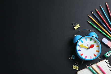 Flat lay composition with alarm clock and different stationery on black background, space for text. school timeの写真素材