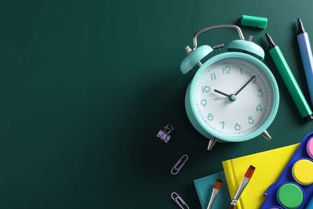 Flat lay composition with alarm clock and different stationery on green background, space for text....