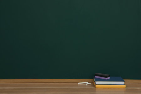 Books, pieces of chalk and duster on wooden table near greenboard, space for textの写真素材