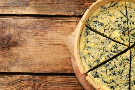 Cut delicious spinach pie on wooden table, top view. Space for text