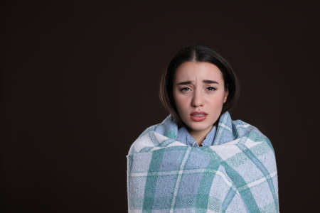 Young woman wrapped in blanket suffering from fever on dark background, space for text. cold symptomsの写真素材