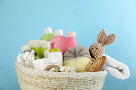 Basket with baby cosmetic products and accessories on light blue background
