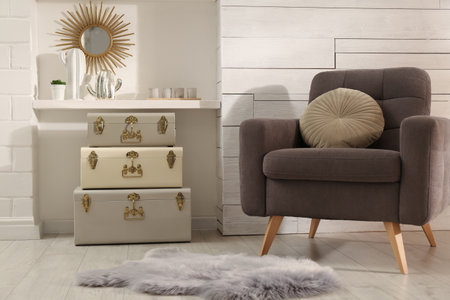 Stylish room interior with comfortable armchair and storage trunks near white wall
