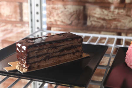 Display case with piece of delicious chocolate cake on shelf in cafe, closeupの写真素材