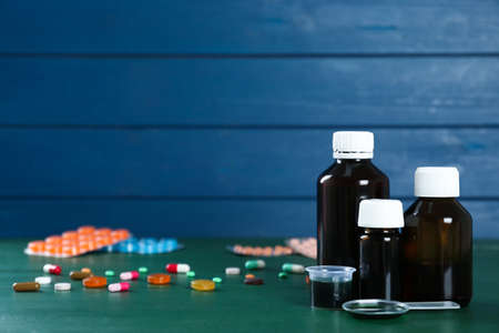Bottles of cough syrup, dosing spoon, measuring cup and pills on green wooden table. Space for textの写真素材