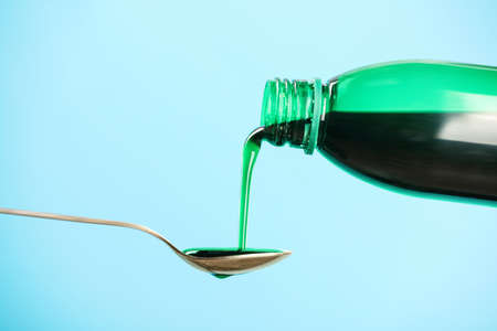 Pouring cough syrup into spoon on turquoise backgroundの写真素材