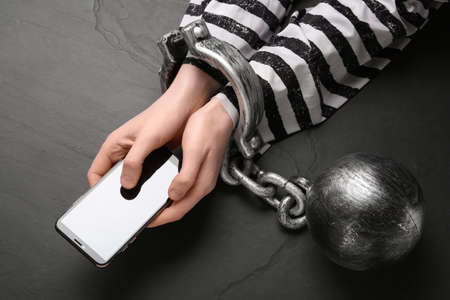Prisoner shackled with ball and chain holding smartphone at black table, top view. internet...