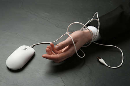 Man tied with computer mouse cable at black table, closeup. internet addictionの写真素材