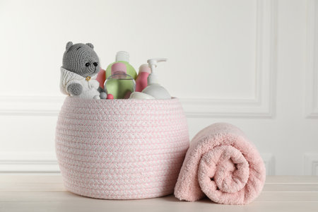 Basket with different baby cosmetic products, towel and toy on white wooden tableの写真素材