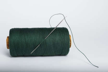 Green sewing thread with needle on white background