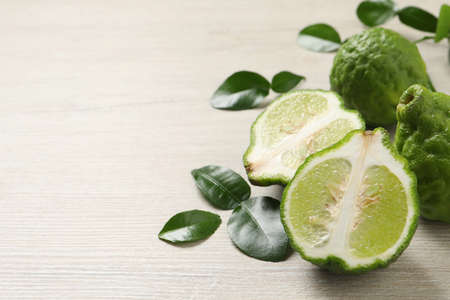 Whole and cut ripe bergamot fruits with green leaves on white wooden table, closeup. Space for textの写真素材