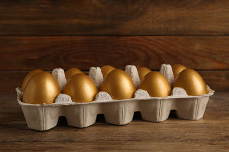 Carton with golden eggs on wooden tableの写真素材