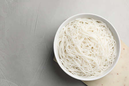 Bowl with cooked rice noodles on light gray table, top view. Space for textの写真素材