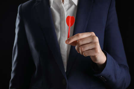 Businesswoman holding red dart on black background, closeupの写真素材