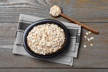 Bowl and spoon with oatmeal on wooden table, flat lay