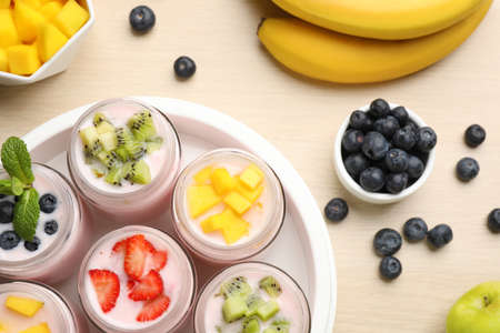 Yogurt maker with jars and different fruits on wooden table, flat layの写真素材