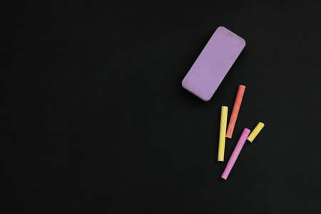Colorful chalks and duster on black board, flat lay. Space for textの写真素材
