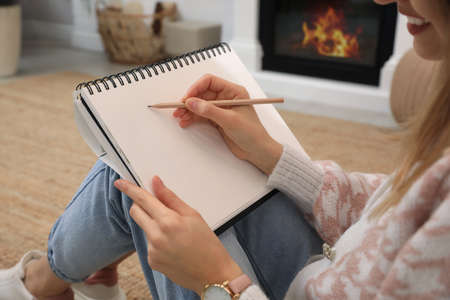 Woman drawing in sketchbook with pencil on floor at home, closeup