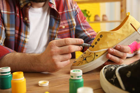 Man painting on sneaker at wooden table indoors, closeup. custom shoes