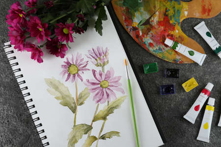 Flat lay composition with beautiful drawing of chrysanthemum flowers in sketchbook on gray tableの写真素材