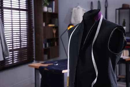 Mannequin with unfinished suit jacket and measuring tape in tailor shop, space for textの写真素材