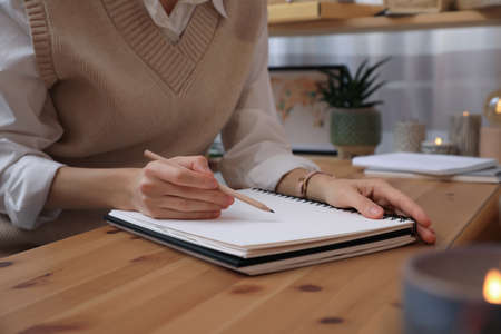 Woman drawing in sketchbook with pencil at wooden table indoors, closeup