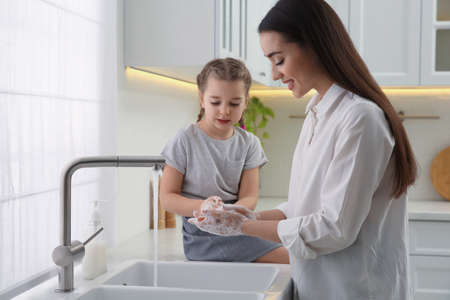 Mother and daughter washing hands with liquid soap in the kitchenの写真素材
