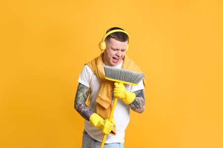 Handsome young man with floor brush singing on orange background