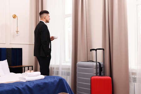 Handsome businessman drinking coffee near window in hotel roomの写真素材