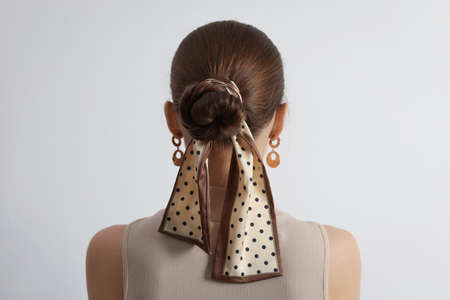 Young woman with stylish bandana on light background, back view