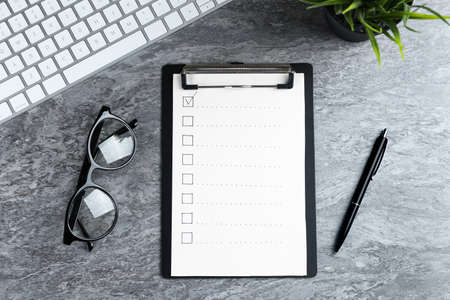Clipboard with checkboxes, computer keyboard, eyeglasses and pen on gray table, flat lay. Checklistの写真素材