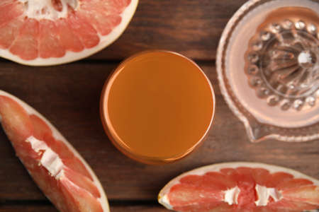 Glass of pink pomelo juice with squeezer and fruit on wooden table, flat layの写真素材