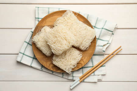 Plate with uncooked rice noodles and chopsticks on white wooden table, flat layの写真素材