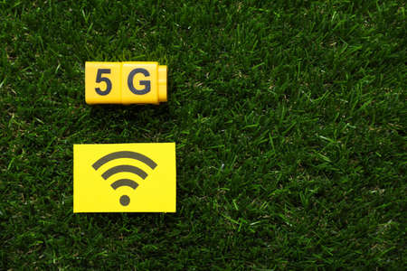 5G technology, Internet concept. Yellow cubes and card with WiFi symbol on green grass, flat lay....