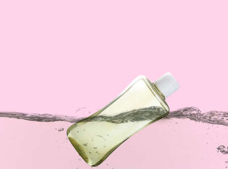 Bottle of baby oil floating in water against pink backgroundの写真素材