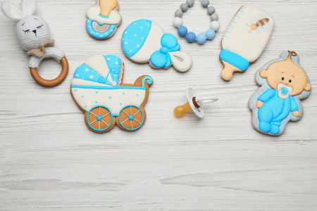 Cute tasty cookies of different shapes, pacifier and space for text on white wooden table, flat lay....