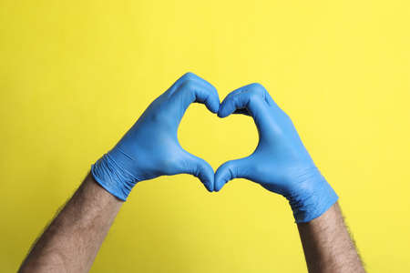 Doctor in medical gloves making heart with hands on yellow background, closeupの写真素材