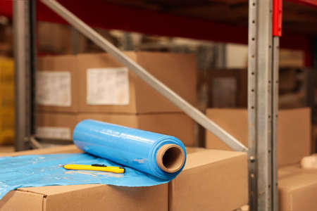 Roll of stretch wrap and utility knife on boxes in warehouse