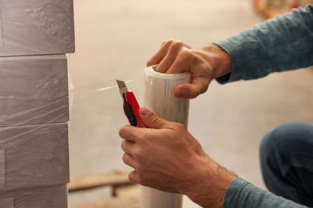 Worker wrapping boxes in stretch film at warehouse, closeup