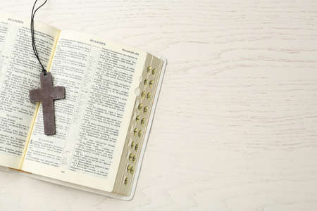 Christian cross and Bible on white wooden table, top view. Space for text