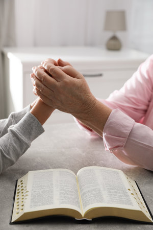 Boy and his godparent praying together at gray table indoors, closeup