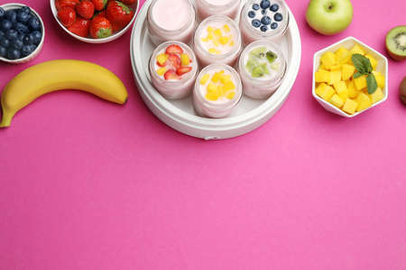 Yogurt maker with jars and different fruits on pink background, flat lay. Space for textの写真素材