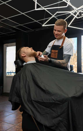 Professional hairdresser working with bearded client in barbershopの写真素材