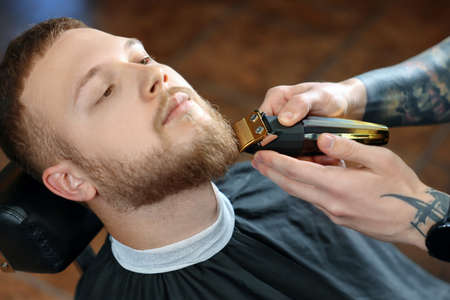 Professional hairdresser working with bearded client in barbershop, closeupの写真素材